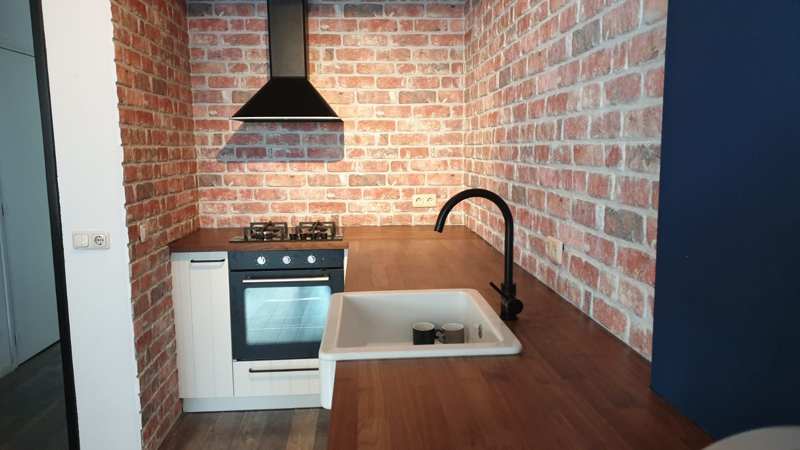 Cuisine avec parement mural brique rouge - plan de travail bois et évier céramique blanc