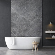 Panneau mural effet marbre gris foncé veiné blanc installé dans une salle de bain moderne avec baignoire îlot
